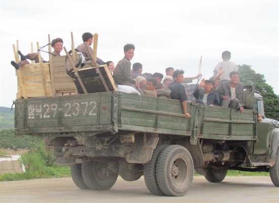 트럭을 타고 가는 북한 주민들. 미소를 지으며 손을 흔들어 준다.