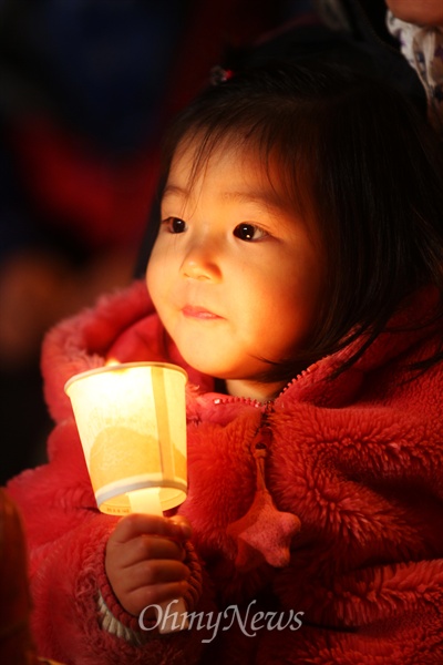 30일 오후 경남 밀양역 광장에서 밀양송전탑 건설을 반대하는 밀양주민과 이를 지지하는 희망버스 참가자들로 열린 문화제 '우리모두가 밀양이다'에 가족들과 함께 나온 아이가 촛불을 들고 있다.