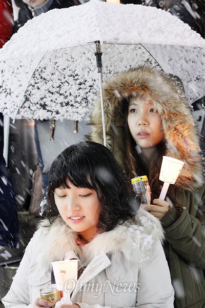 대선 1주년을 맞은 19일 오후 7시 광주 동구 충장로 우체국에선 시민 50여 명이 참여한 가운데 대선 1주년 촛불문화제가 열렸다. 문화제에 참석한 대학생 두 명이 우산을 나눠쓴 채 눈을 피하고 있다.