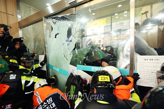 지난해 12월 22일 민주노총이 입주한 경향신문사 1층 현관 유리문을 열기위해 장비를 든 소방대원들이 투입되어 경찰이 노동자들이 막고 있던 유리문을 깨고 진입을 시도하고 있다.