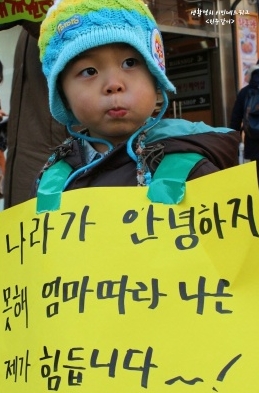 엄마 따라온 꼬마가 안녕하지 못한 이유('나라가 안녕하지 못해 엄마 따라 나온 저도 힘듭니다')를 적은 손팻말을 들고 있다.