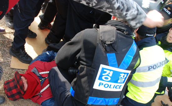 전신주와 자신의 목에 밧줄을 연결한 주민을 경찰이 왼쪽 무릎으로 짓누르고 밧줄을 자르고 있다.
