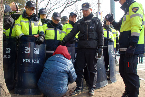 할머니 한 분이 경찰에 포위된 주민을 만나게 해달라고 요구하다 지쳐서 경찰의 다리 밑으로 들어가 보려고 한다.