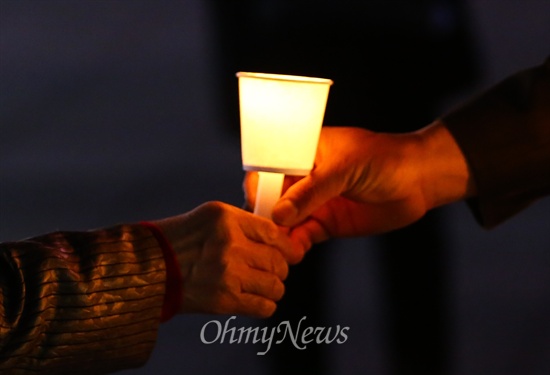 세월호 침몰사건 1주일째인 22일 오후 경기도 안산문화광장에서 열린 실종자 무사귀환과 희생자 추모를 위한 촛불문화제에서 한 참가자가 촛불을 건내 받고 있다.