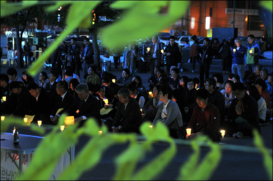 시민들이 매달아 놓은 '세월호 무사생환 염원 노란리본' 사이로 촛불에 참여한 시민들이 앉아 있다.