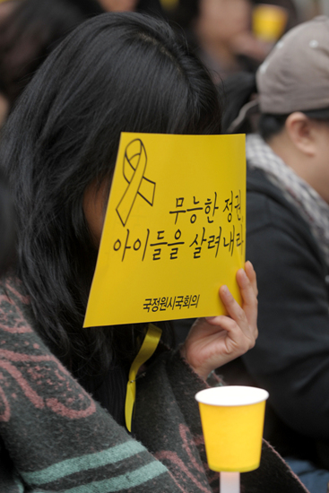 26일 오후 서울 광화문 동화면세점 앞에서 한 시민이 '세월호 침몰사고'로 인한 희생자들을 애도하는 기도가 진행되는 가운데 피켓으로 얼굴을 가린 채 흐느끼고 있다.