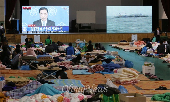 정홍원 국무총리는 27일 오전 서울 세종로 정부중앙청사에서 세월호 침몰 사고와 관련해 긴급기자회견을 열고 "진작 책임을 지고 물러나고자 했으나 우선은 사고 수습이 급선무이고 하루 빨리 사고 수습과 함께 대책을 마련하는 것이 책임있는 자세라고 생각했다"며 "그러나 이제 더 이상 제가 자리를 지킴으로써 국정운영에 부담을 줄 수 없다는 생각에 사퇴할 것을 결심했다"고 밝혔다. 전남 진도 실내체육관에서 실종자 가족들이 생중계 화면으로 정 총리의 회견을 지켜보고 있다. 오른쪽에는 사고해역 수색현황을 보여주는 모니터 화면이 켜져 있다.