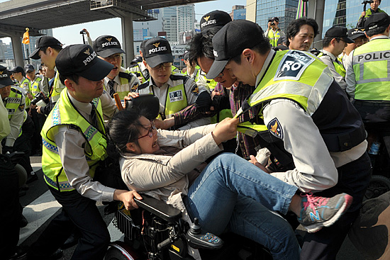  '2014년 세계노동절대회'를 끝마친후 거리행진을 시도하는 장애인들과 이를 저지하는 경찰들이 충돌하는 과정에서 경찰들이 여성 장애인이 탄 휠체어를 들어 이동시키고 있다.
