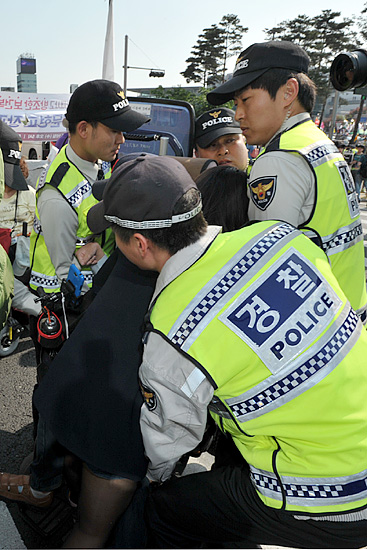  '2014년 세계노동절대회'를 끝마친후 거리행진을 시도하는 장애인들과 이를 저지하는 경찰들이 충돌하는 과정에서 경찰들이 여성 장애인이 탄 휠체어를 들어 이동시키려 하자 한 여성봉사자가 경찰들을 막고있다.