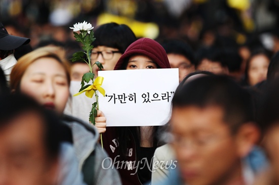 3일 오후 서울 청계천광장에서 열린 세월호 침몰사고 희생자 추모와 실종자 무사귀환을 위한 국민촛불 집회에 한 참가자가 세월호 선내 방송을 뜻하는 '가만히 있으라' 손피켓과 국화꽃을 들고 있다.