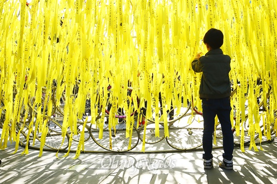 지난 3일 오후 서울 광화문 청계광장에 설치된 세월호 침몰희생자들의 추모하는 조형물 <못다핀 꽃>에 한 어린이가 노란 리본을 달고 있다.