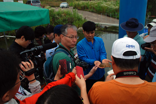 환경운동연합 염형철 총장이 함안보 선착장에서 발견한 큰빗이끼벌레를 들어 보이자 취재진이 몰렸다. 정민걸 교수(왼쪽 안경 쓴 인물)가 설명하고 있다.