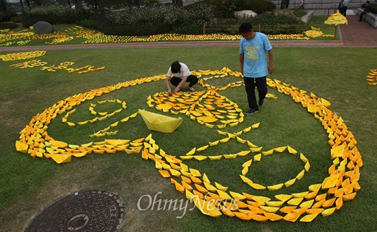 세월호 침몰사고 유가족이 14일 오전 서울 여의도 국회 본청 앞 잔디밭에서 세월호 침몰사고를 잊지 말자는 의미로 수십 개의 노란종이배로 하트를 만들어 보이고 있다. 