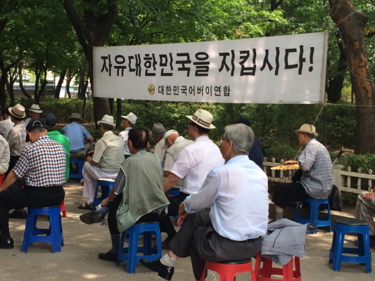 자유대한민국을 지킵시다 어버이연합에서 주최하는 연설회를 듣고있는 어버이연합 회원들 머리 위로 어버이 연합의 현수막이 보인다