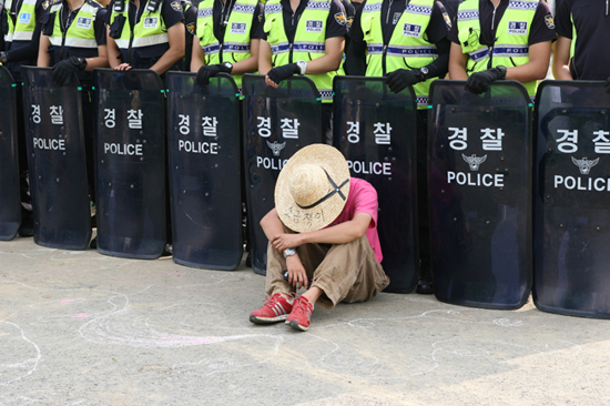 청도 송전탑 건설에 반대하는 농성자가 수십 명의 경찰 병력 앞에 쪼그려 앉아 있는 모습. 경찰 뒤로는 송전탑 공사에 투입되는 인력이 울타리를 쳐놓고 숙식을 해결하고 있다.