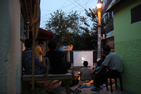 수요일 저녁 8시, 영화 ‘미워도 다시 한 번’ 상영을 보기 위해 마을사람들이 골목에 모여 앉았다.
