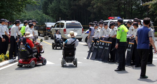 충북장애인차별철폐연대 일부 회원들이 휠체어를 타고 음성 꽃동네 행사장 입구로 가려다 경찰에 의해 저지당하고 있다.