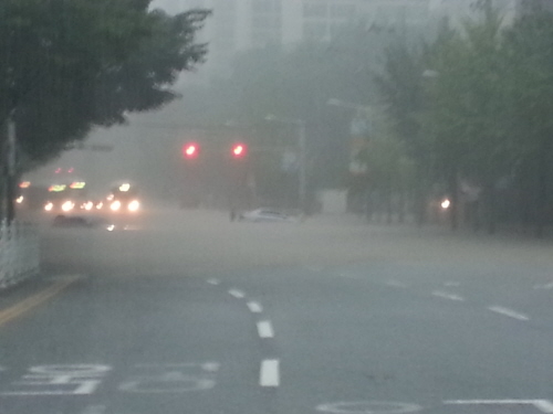 부산은행 화명대천영업소 앞 도로(금곡대로). 폭우에 불어난 물에 순식간에 승용차가 고립되었다. 5분 전에도 차량이 지나가고 있었다. 사진은 오후 2시 30분쯤의 상황이다. 