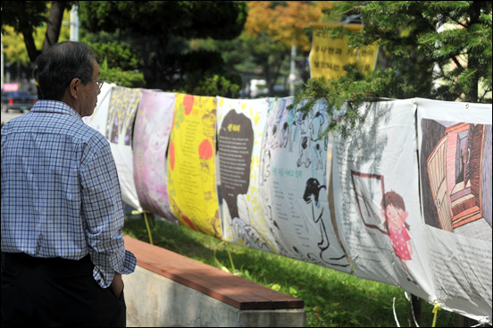 대전시청 북문 앞 거리에 전시된 ‘한뼘 그림책 세월호이야기’ 전시 작품을 지나가던 시민이 바라보고 있다.