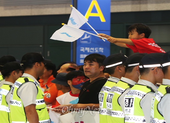 경찰 장벽 너머 한반도기 흔드는 어린이 2014 인천아시안게임에 참가하는 장수명 북한올림픽위원회 대표와 축구·조정 선수와 심판, 기자단 등 1진 94명이 11일 오후 고려항공을 이용해 인천공항에 도착했다. 아빠 어깨에 올라 탄 한 어린이가 경찰 장벽 너머 한반도기를 흔들며 북한선수단을 환영하고 있다.
