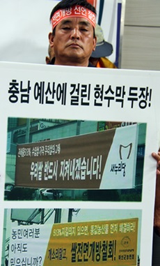 한 농민이 최근 충남 예산에 걸린 새누리당의 현수막 사진을 들어 보이고 있다. 현수막에는 '우리쌀 반드시 지켜내겠습니다'라고 새겨 있다.