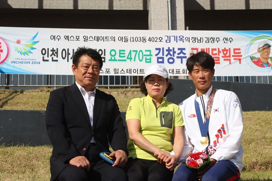  김창주 선수의 아버지 김기옥(56세)씨와 엄마 김경자(55세)씨가 아파트 입주민들이 내건 축하펼침막 앞에서 기념 사진을 찍고 있다.