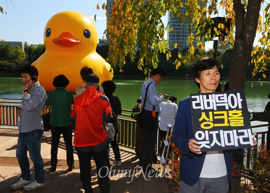 14일 오후 서울 송파구 석촌호수에 떠 있는 네덜란드 예술가 플로렌타인의 작품 러버덕(Rubber Duck)' 앞에서 한 시민이 '러버덕아 싱크홀 잊지마라'가 쓰여진 피켓을 들고 1인 시위를 벌이고 있다. 