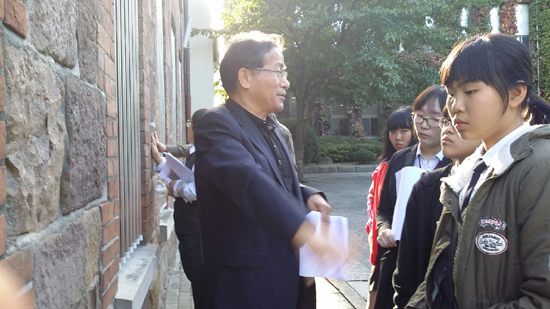 계성학교 아담스관의 벽에 석재로 대구읍성의 성벽 돌을 설명하고 있는 정만진 한국예술인복지재단 파견예술인. 일부 학생들은 손으로 성벽돌을 만져보고 있다.