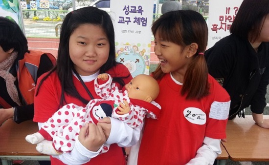 여학생들이 신체건강 체험마당의 성교육 부스에서 아기 인형을 예뻐하고 있다.