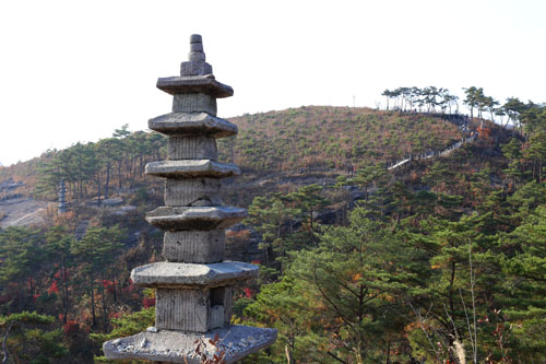  운주사의 석탑과 천불천탑길. 여행객들이 산등성이의 와불을 보고 길을 따라 내려오고 있다.