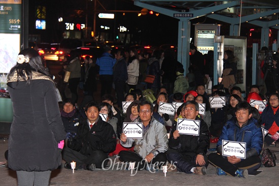 19일 저녁 창원 정우상가 앞에서 열린 "근조 민주주의, 민주수호 경남촛불문화제"에서 참가자들이 촛불과 피켓을 들고 노래 공연을 들으며 앉아 있다.