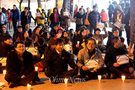  19일 저녁 창원 정우상가 앞에서 열린 "근조 민주주의, 민주수호 경남촛불문화제"에서 참가자들이 촛불과 피켓을 들고 앉아 있다.