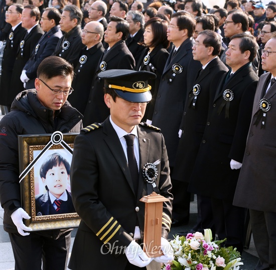 세월호 참사로 조카 잃은 지성진씨, 마지막 배웅 세월호 참사로 외조카를 잃은 지성진씨가 27일 인천광역시청 앞 미래광장에서 엄수된 세월호 사고 일반인 희생자 합동영결식에서 조카의 영정을 들고 장지로 향하고 있다. 정홍원 국무총리와 정종섭 행정자치부 장관, 박인용 국민안전처 장관, 조윤선 청와대 정무수석, 박원순 서울시장, 유정복 인천시장 등 정부측 인사들이 이들 영정 행렬을 말없이 지켜보고 있다.