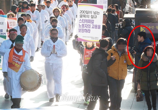 금속노조 쌍용자동차 해고노동자와 연대 단체 참가자들이 지난 7일 오전 서울 구로구 쌍용자동차 구로정비사업소 앞에서 정리해고 비정규직법제도 전면폐기를 위한 2차 오체투지 행진을 벌이고 있는 가운데, 카메라를 든 구로경찰서 정보과 소속 경찰(붉은 색 표시) 몸을 숨기며 행진단을 주시하고 있다.