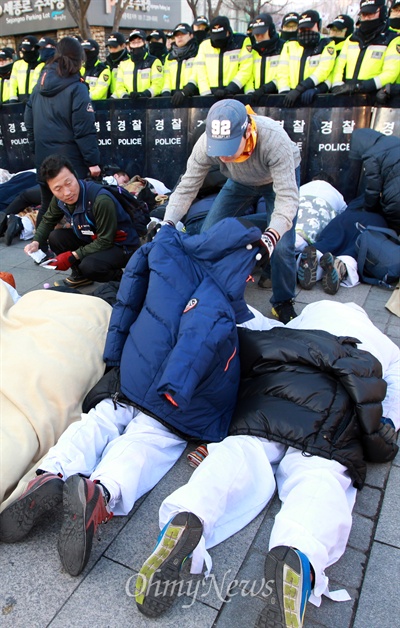금속노조 쌍용자동차 해고노동자와 연대단체 참가자들이 11일 오후 서울 종로구 정부서울청사 앞에서 비정규직 법·제도 철폐를 요구하며 2시간 넘게 차가운 바닥에 엎드려 있자, 시민들이 이들의 몸을 걱정하며 입고 있던 잠바를 벗어 덮어주고 있다.