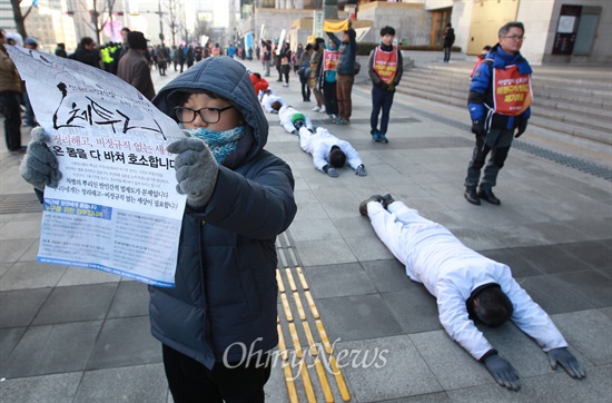 금속노조 쌍용자동차 해고노동자와 연대단체 참가자들이 2015년 1월 11일 오후 서울 종로구 세종문화회관을 지나며 비정규직 법·제도 철폐를 요구하는 오체투지를 벌이자, 부모님과 함께 온 학생이 이들을 응원하며 유인물을 들어보이고 있다.