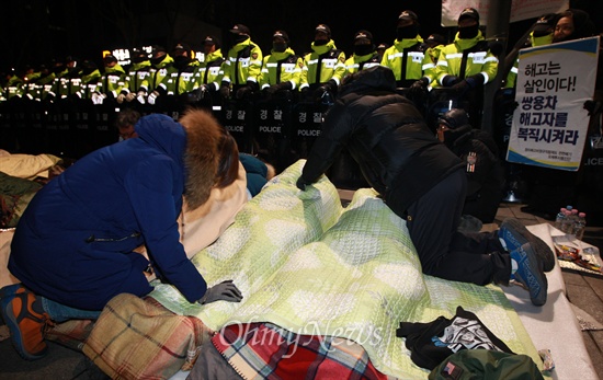 금속노조 쌍용자동차 해고노동자와 연대단체 참가자들이 12일 오전 서울 종로구 정부서울청사 앞에서 경찰 막혀 밤을 보내자, 시민들이 이들의 건강을 걱정하며 하루종일 차가운 바닥에 엎드려 뭉친 근육을 풀어주고 있다.