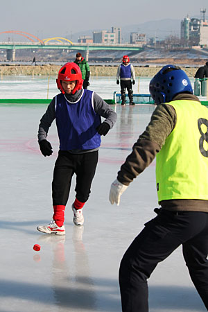 빙판 위에서 벌어지는 얼음축구대회. 나무로 만든 빨간 공을 사이에 두고 공격하는 선수와 수비하는 선수 사이에 팽팽한 긴장감이 감돈다.