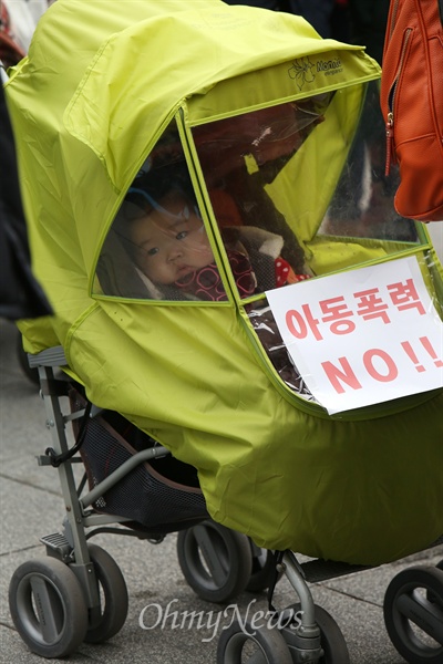 한 어린이가 타고 있는 유모차에 구호가 적힌 손피켓이 놓여 있다.