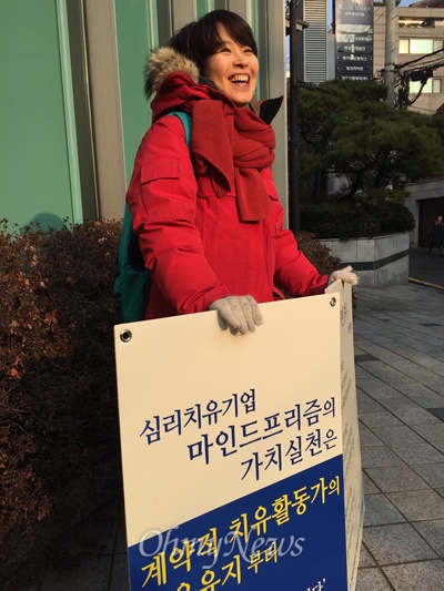19일 오전 서울 역삼동 마인드프리즘 사무실 앞에서 복직을 요구하는 1인 시위를 벌이고 있는 마음 치유사 김미성씨가 자신을 지켜보는 동료들을 향해 밝게 웃고 있다.