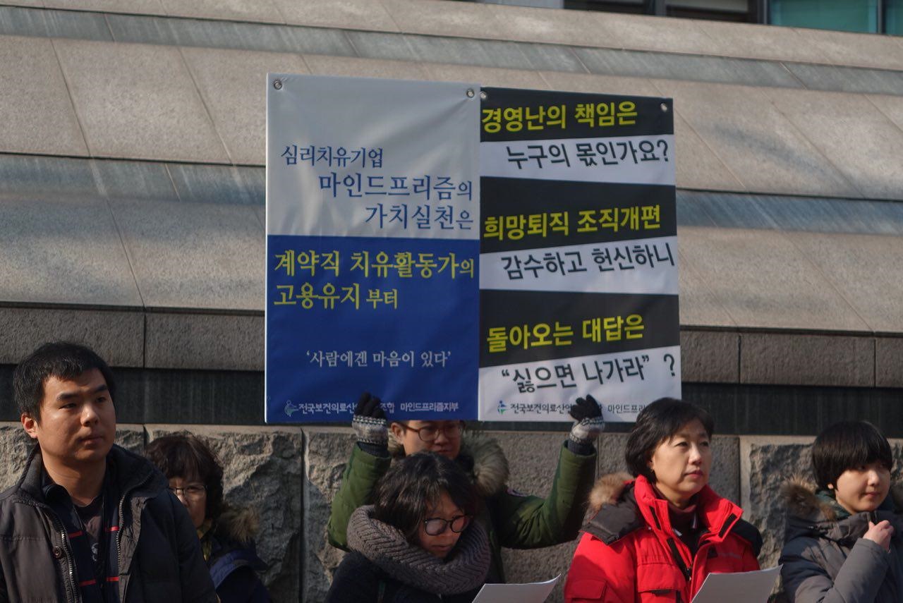 보건의료노조 마인드프리즘지부와 시민단체가 주최한 기자회견에서 참가자가 피켓을 들고 있다.