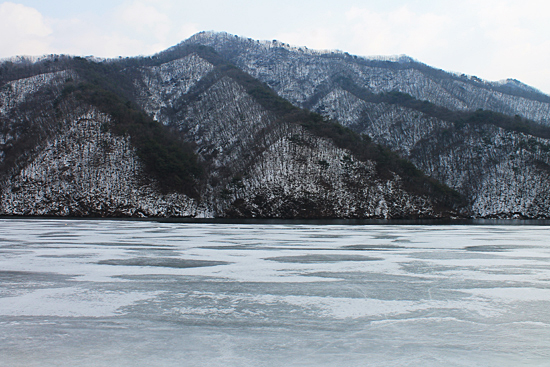 얼어붙은 강 표면이 서서히 녹고 있는 풍경. 뒷산 배경이 일월오봉도를 연상시킨다.