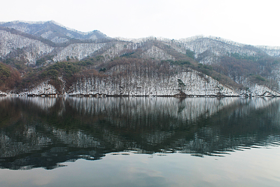 산 그림자가 얼음이 녹은 강물 위에 비쳐 완전히 대칭을 이루고 있는 풍경.