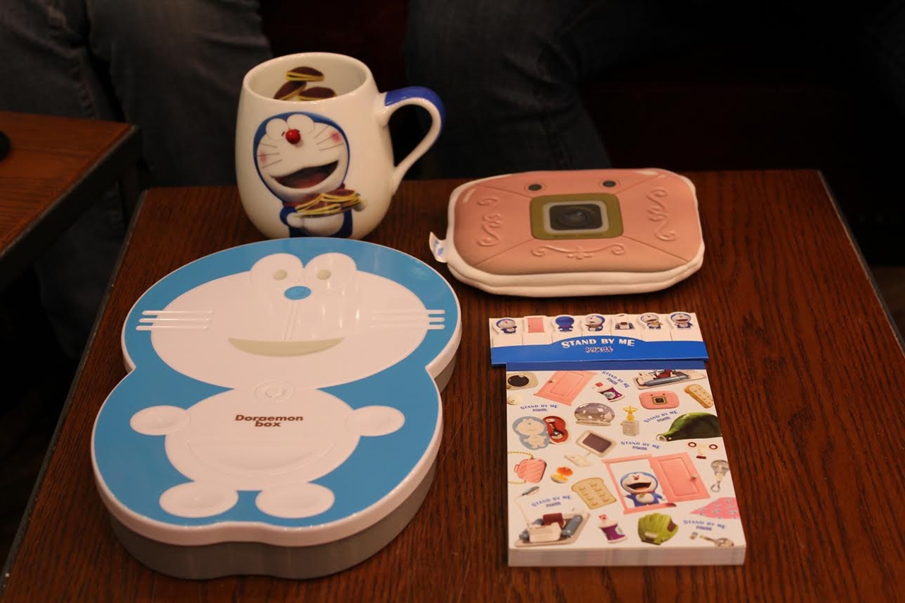  도라포켓 씨가 최근 구입한 도라에몽 관련 상품들. (왼쪽 상단부터 시계방향) 한정판 컵과 카메라 모양의 파우치, 메모지, <도라에몽: 스탠 바이 미> 한정판 블루레이.