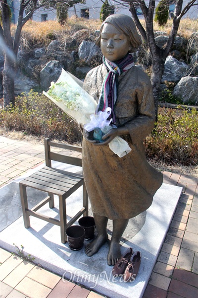 경남 거제문화예술회관 소공원에 있는 '평화의 소녀상'에 꽃다발이 안겨져 있고, 목도리가 둘러져 있으며, 신발이 놓여져 있다.