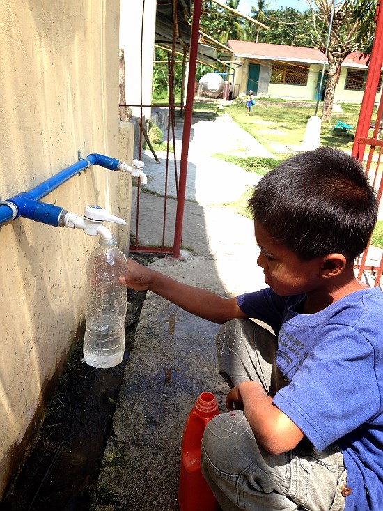 빗물 음용시설에서 한 아이가 페트병에 물을 담고 있다. 