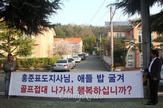  친환경무상급식지키기 경남운동본부 소속 학부모들이 30일 아침 홍준표 경남지사의 관사 앞 골목에서 '무상급식 지원 중단'과 '해외골프'에 항의하며 펼침막을 들고 서 있다.