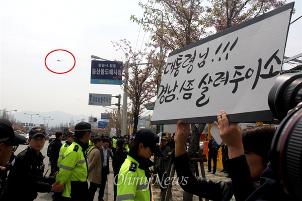 박근혜 대통령이 9일 오전 경남 창원을 방문한 가운데, 학부모들이 행사장 입구 도로가에 무상급식 재개를 바라는 내용의 피켓을 들고 서 있어 그 주변에 경찰이 지키고 서 있다. 사진은 박근혜 대통령이 탄 것으로 추정되는 헬리콥터(원안)가 상공을 지나고 있는 모습.
