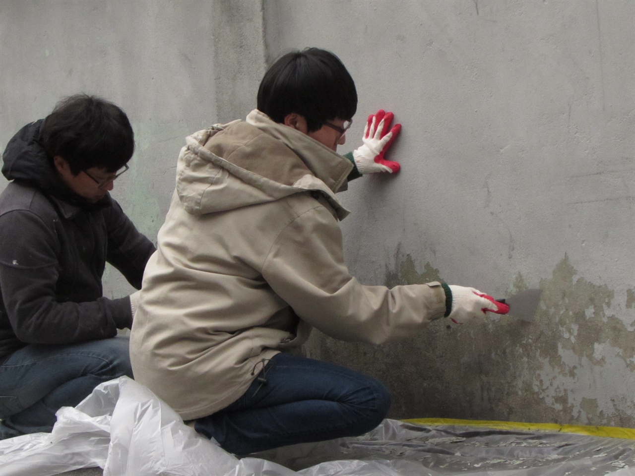 낡은 벽의 이물질을 긁어내고 벽화그리기에 필요한 바탕작업을 하는 청년들.