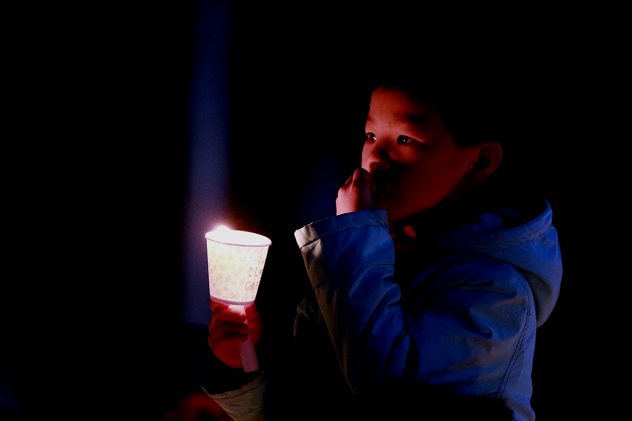 행사장 바같에서 부모와 함께 참여한 어린이가 촛불을 밝히고 있다.